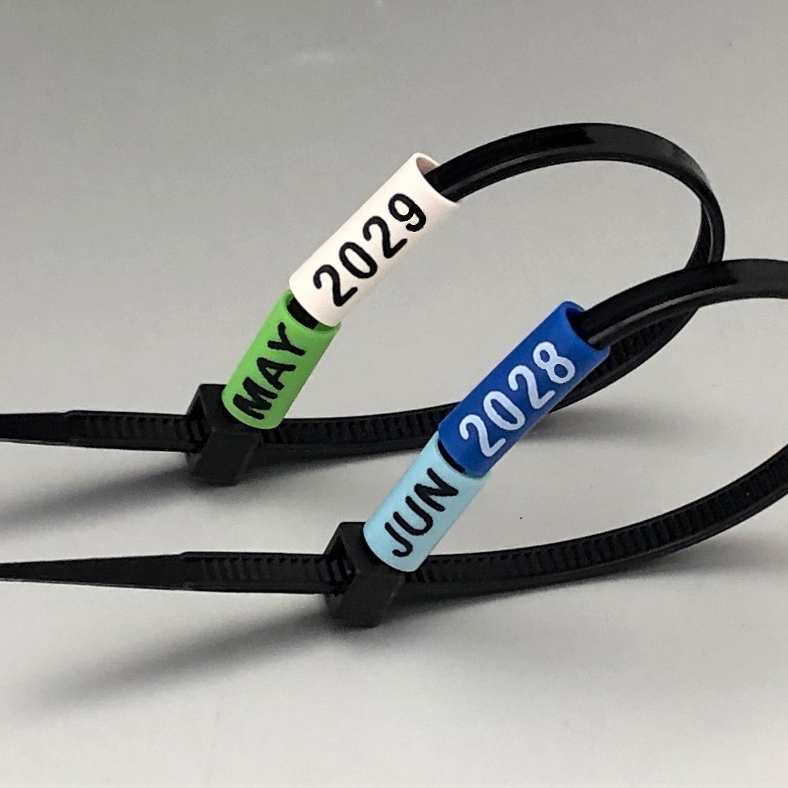 Black zip tie with date labels 'May 2029', 'June 2028' on a gray background by www.cablelabels.uk