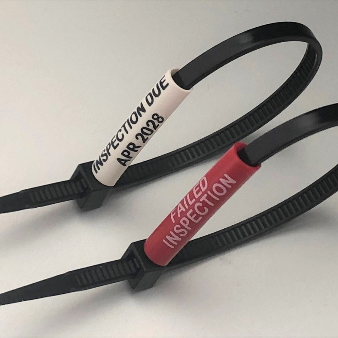 Two black cable ties with inspection labels on a white background by www.cablelabels.uk