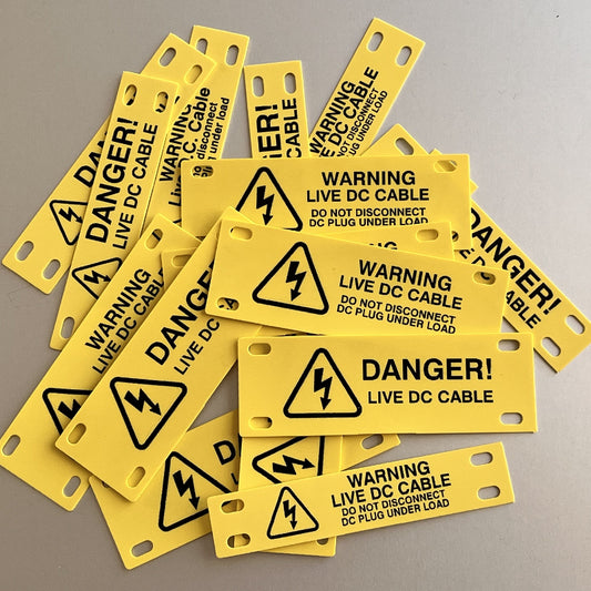 Multiple yellow warning labels with black text and symbols on a gray background by www.cablelabels.uk